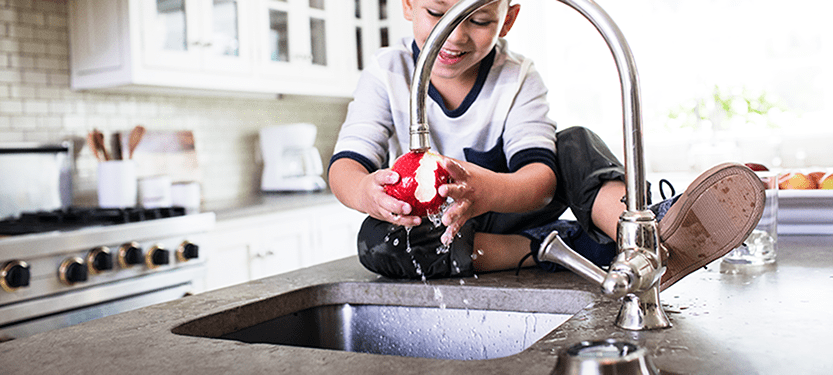 Boy rinsing apple under faucet with Culligan water